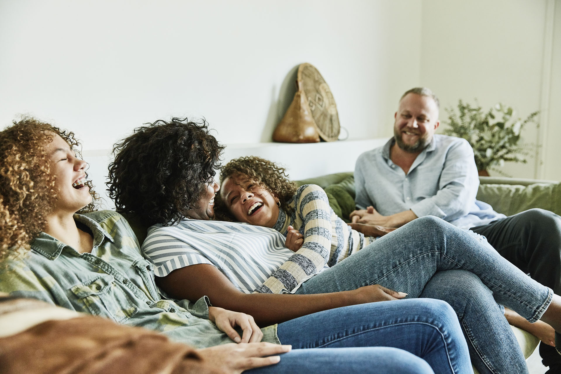 Laughing daughter embracing mother while sitting on couch with family in living room